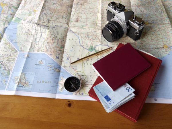 Camera, passport, compass, notebook, golden pen and 20€ bills on top of a map